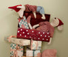 The Maileg Christmas Mouse, Maxi - Girl wears a red dress and sits with festive accessories in a red polka-dot suitcase atop pastel-wrapped presents, adding holiday cheer against a light green wall.