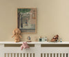 A nursery shelf displays soft fabric plush toys, a Maileg Lion, Mini from the safari friends collection, a miniature kitchen set, and small figurines. Above, a framed illustration shows "louimax Dreams of Being an Adult.