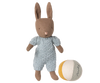 The Maileg Micro Bunny With Ball - Brown - Blue (With Magnetic Hands) wears a light blue knitted outfit and stands next to a small soft ball with white, yellow, and gray panels on a plain background.