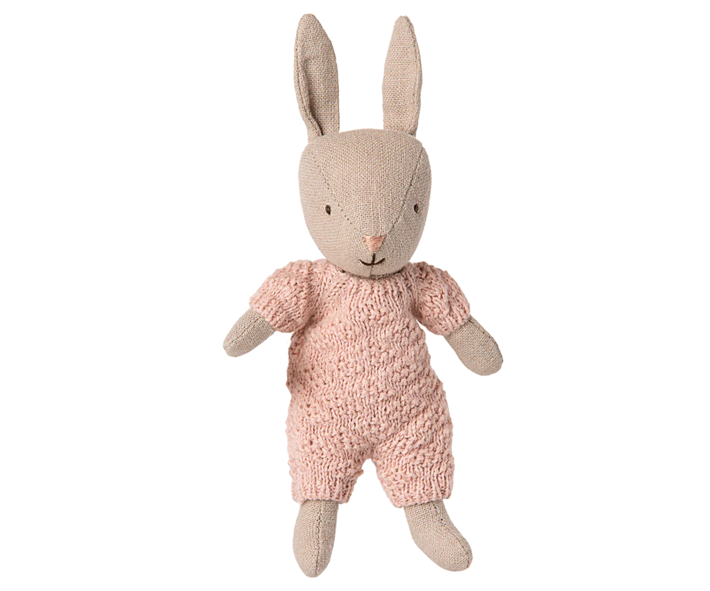 A beige fabric bunny doll wears the Maileg Extra Clothing: Knitted Suit, Micro - Rose—a pink knitted outfit for Micro Bunny—featuring long upright ears and a simple embroidered face, set against a plain white background.