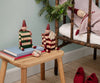 A Maileg Elf with Drawer - Green (pre-order, arriving mid August) sits on a wooden stool near a gift box and books, while another elf in red and white rests on a rustic bed with red shoes and a pine branch nearby.