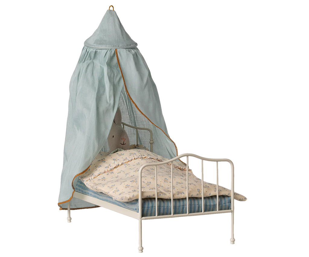 The Maileg Bed Canopy, Miniature - Mint (expected 04/15/26) is a small white metal canopy bed with blue-striped bedding, a floral blanket, sheer cotton mint canopy, and a plush rabbit—ideal for romantic bedroom decor.