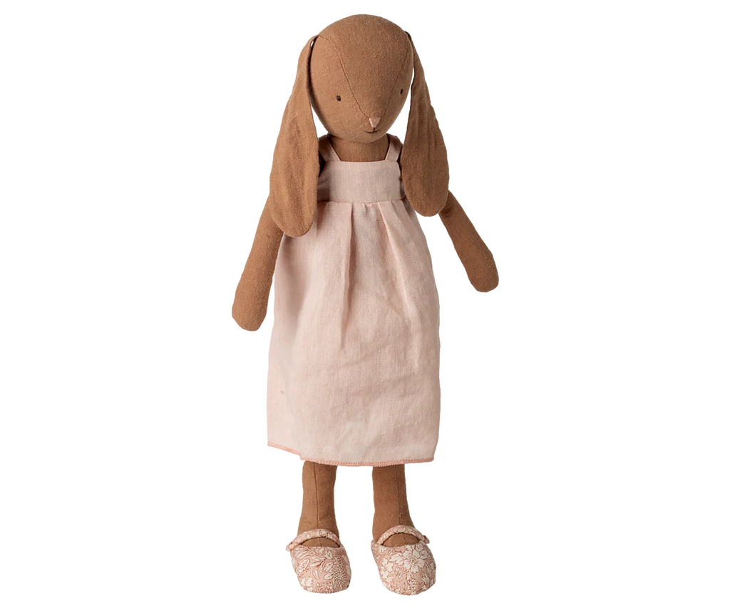 The Maileg Bunny, Size 3, in chocolate brown stands upright in a light pink dress and matching shoes against a white background.