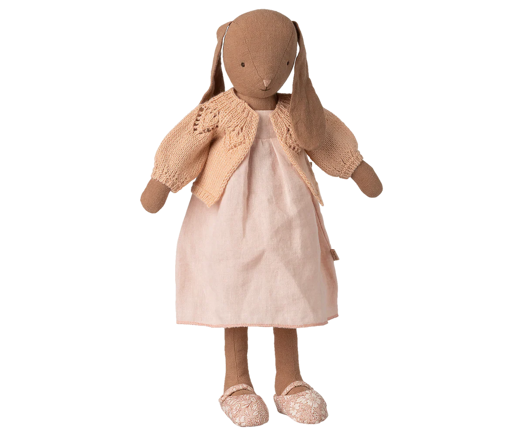 A stuffed brown bunny doll stands upright against a white background, dressed in adorable bunny clothes—a pale pink dress, matching pink slippers, and the Maileg Knitted Cardigan, Size 3 - Light Rose (expected 02/15/26).
