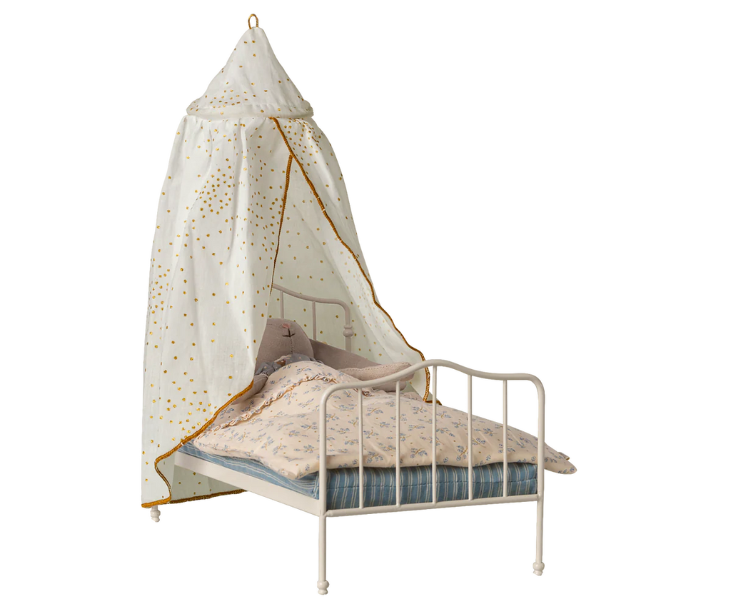 A charming bedroom scene featuring a white metal child's bed with floral bedding, a blue striped blanket, and the Maileg Bed Canopy, Miniature - Off-White (arriving 04/15/26), adding whimsical elegance to the decor.