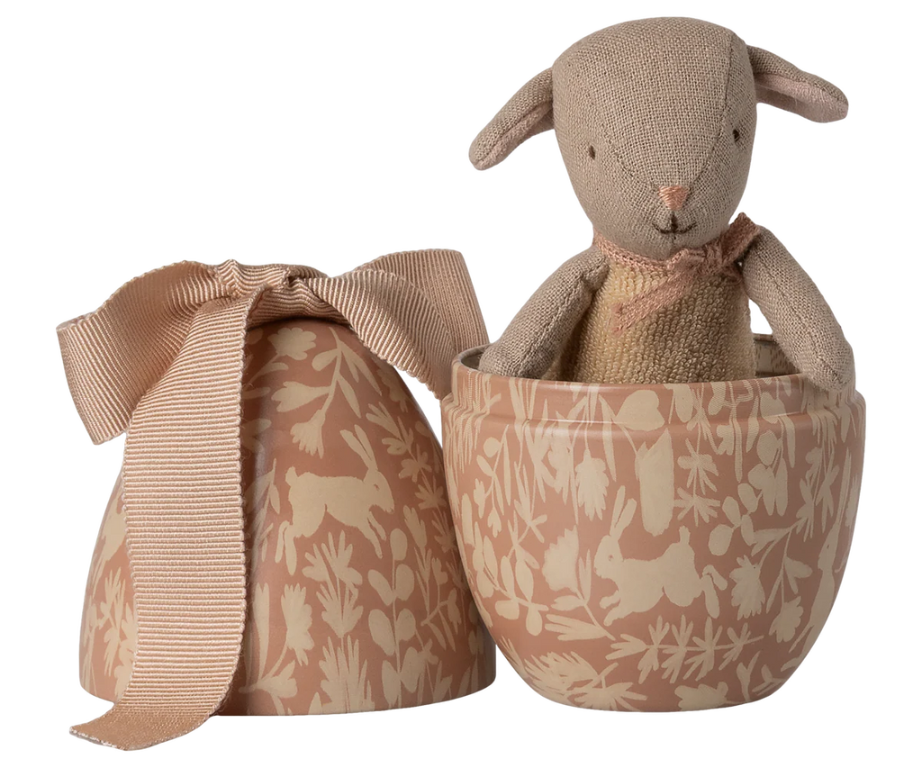 The Maileg Easter Egg with Micro Lamb, Small - Powder features a soft brown plush lamb in a decorative tan egg-shaped container with a nature design and ribbon-topped lid, making a charming gift.