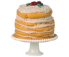 The Maileg Party Cake and Cake Stand, Mouse - Off White (Expected arrival: 05/01/26) features a tall layered yellow sponge cake with white frosting and red-blue fruit decorations, displayed on a fluted white stand as the party centerpiece.