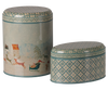 PRE-ORDER: Maileg Metal Box Set - Santa is Coming includes two decorative Christmas boxes—one cylindrical, one oval. Both feature blue and gold patterned lids and borders; the larger metal box shows Santa’s sleigh with reindeer in a snowy scene.