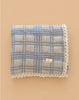 The Organic Cotton Baby Quilt - French Plaid, Bluebelle is a 30x40 inch blue checkered quilt with white lace trim, made from organic cotton in Portugal and shown on a beige background.