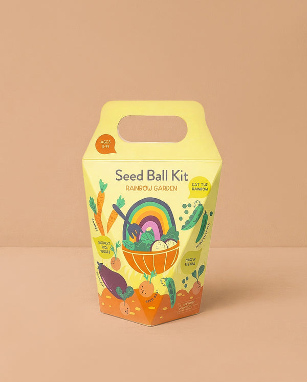 The DIY Seed Ball Kit - Rainbow Garden comes in a yellow and orange box with a handle, featuring colorful veggies, a rainbow, smiling seed balls, and notes Non-GMO Seeds. It's a fun STEM activity for ages 3+.