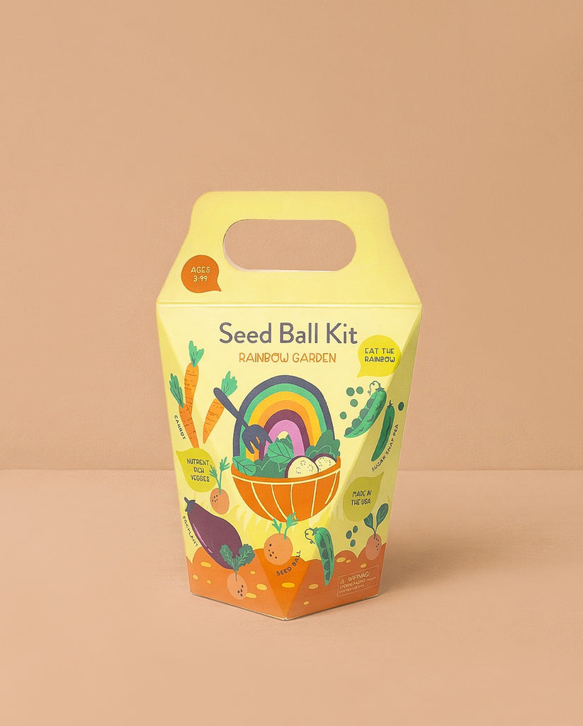 The DIY Seed Ball Kit - Rainbow Garden comes in a yellow and orange box with a handle, featuring colorful veggies, a rainbow, smiling seed balls, and notes Non-GMO Seeds. It's a fun STEM activity for ages 3+.