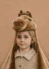 A young child with light hair wears the Costume - Brown Horse, featuring a plush brown horse hat with ears and mane, paired with a beige button-up shirt, standing against a plain tan background.