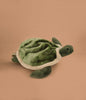 The Children's Backpack - Turtle is a green and white plush bag with a soft shell, flippers, and adjustable shoulder straps, shown on a plain tan background.