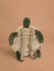 The Children's Backpack - Turtle features green flippers and head, a beige shell, adjustable straps, and is displayed on a tan background with its back and zipper showing.