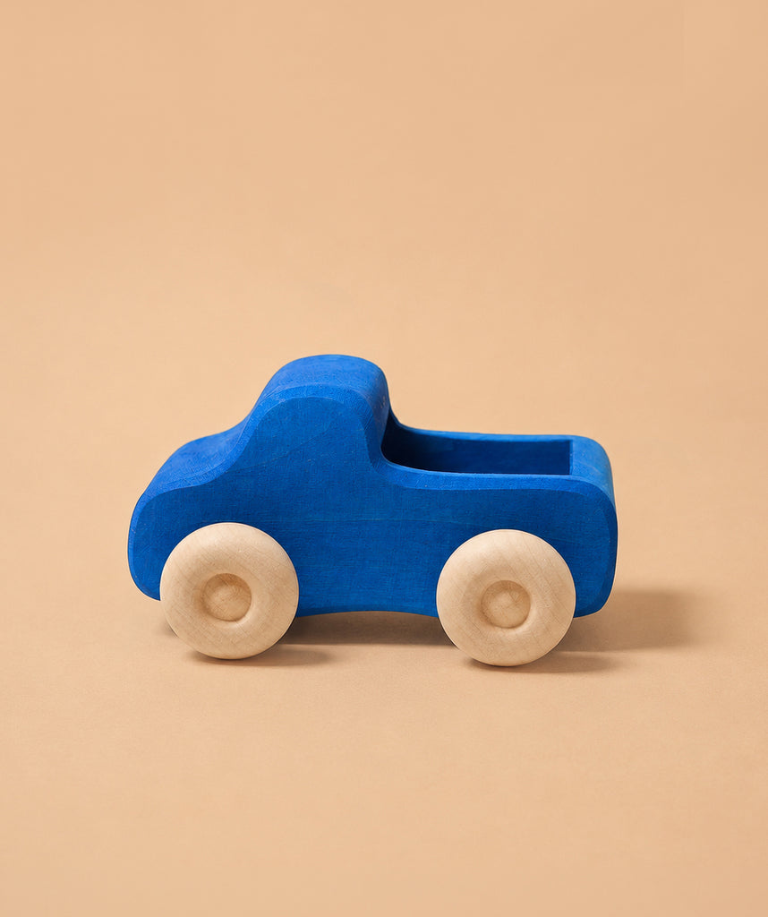 Grimm's Small Blue Truck, a non-toxic wooden toy with natural wood wheels and a blue body, sits on a plain beige background.