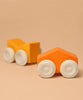 Two Grimm's Stacking Cars - Orange, wooden toy cars with white wheels in bright orange and yellow-orange, are displayed on a beige surface with a matching beige background.