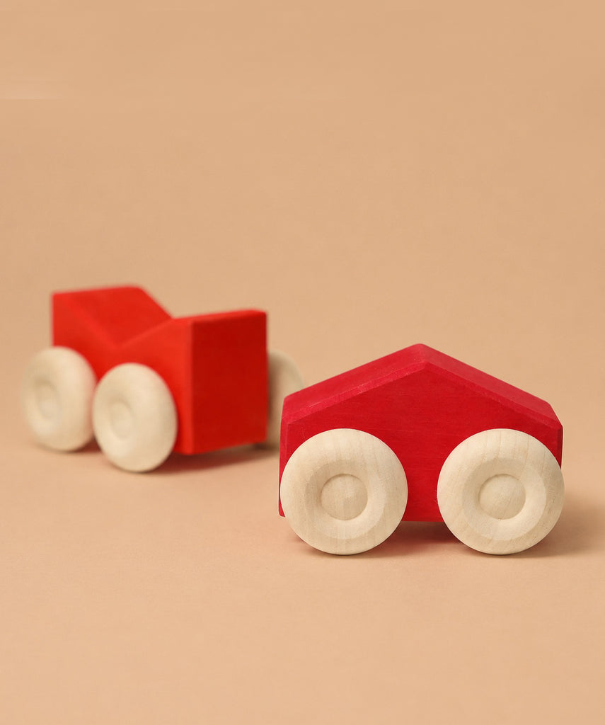 Two simple wooden Grimm's Stacking Cars - Red, featuring white wheels and angular shapes, are showcased on a beige surface with a matching background—ideal for color matching or stacking play.