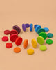 Grimm's Wooden Rainbow Coins arranged in a spiral, showing a color gradient from red, orange, yellow, green, blue to purple on a beige background.