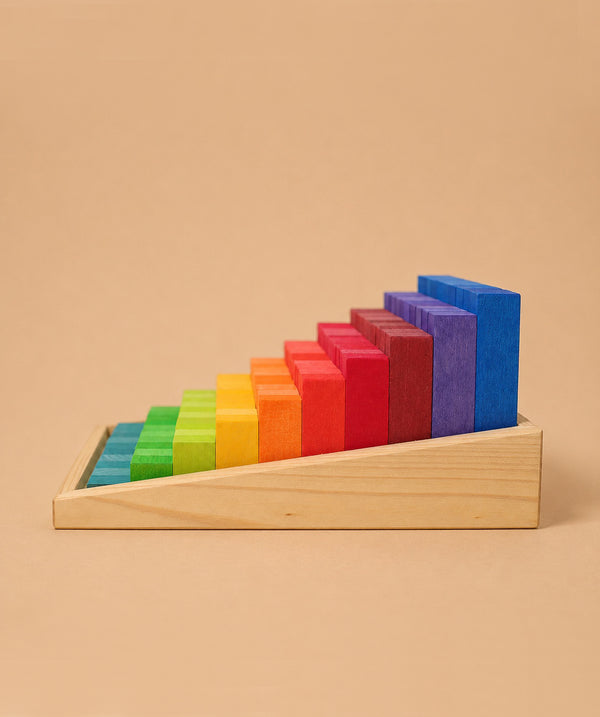 Grimm's Stepped Counting Blocks - Small features natural wooden blocks in a rainbow gradient, arranged by size in a slanted wooden tray against a beige background.