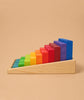 Grimm's Stepped Counting Blocks - Small features natural wooden blocks in a rainbow gradient, arranged by size in a slanted wooden tray against a beige background.