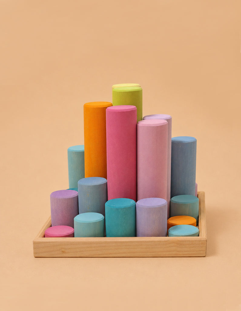 Grimm's Large Building Rollers - Pastel features colorful, cylindrical stacking pieces in varying heights neatly arranged in a wooden tray, creating a pastel gradient and adding playful charm against a beige background.