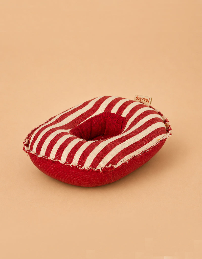 A plush, red and white striped donut-shaped cushion, featuring a small label and set against a beige background—perfect as an accessory for your Maileg Rubber Boat, Small Mouse - Red Stripe, or as a cozy resting place for playful mice.