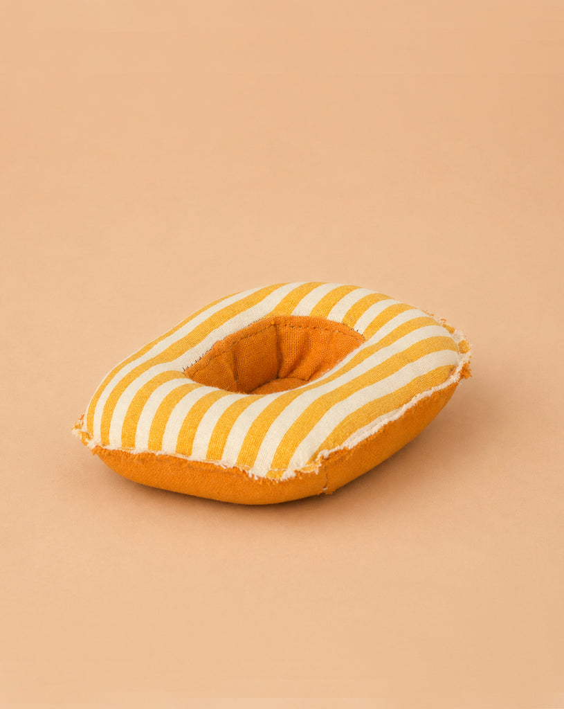 A soft, round yellow and white striped Maileg Rubber Boat for Small Mouse, featuring a central hole reminiscent of a donut, rests on a light tan background—perfect as a charming accessory for Maileg mice or as an adorable pretend boat for imaginative playtime adventures.