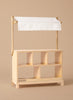 The Milton & Goose Market Stand, handcrafted in the USA, features six open cubby shelves and a white fabric canopy—ideal for pretend play—shown here against a plain beige background.