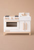 The Milton & Goose Essential Play Kitchen—made in the USA—features a white stove with four burners, an oven with a clear window, a sink and faucet, and wooden handles. Perfect for imaginative play against a beige background.