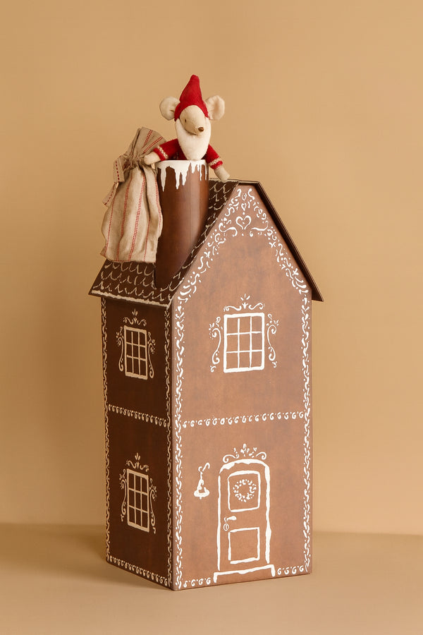 A small toy mouse in a red hat and striped sack sits in a chimney atop the Maileg Cardboard Two-Story Gingerbread House with white icing-like designs, ideal for Advent gifts, set against a plain beige background.
