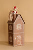 A small toy mouse in a red hat and striped sack sits in a chimney atop the Maileg Cardboard Two-Story Gingerbread House with white icing-like designs, ideal for Advent gifts, set against a plain beige background.
