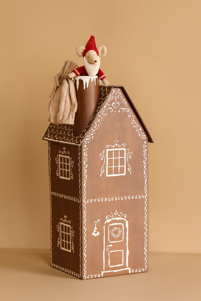 A small toy mouse in a red hat and striped sack sits in a chimney atop the Maileg Cardboard Two-Story Gingerbread House with white icing-like designs, ideal for Advent gifts, set against a plain beige background.