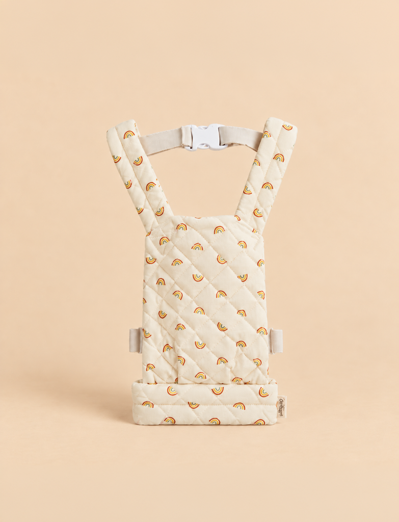 Olli Ella Quilted Doll Carrier - Rainbow, a soft, cream-colored doll carrier featuring a quilted texture and a pattern of small rainbows, shown upright against a matching beige background.