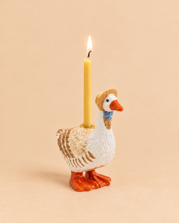 A charming handcrafted “Mother Goose Cake Topper” features a ceramic goose with a blue bow and tan hat, standing on an orange base with a yellow candle glowing on its back against a beige background—perfect as a birthday decoration or collectible keepsake.
