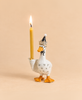 Introducing the Goodnight Goose Cake Topper – Final Sale: This handcrafted collectible ceramic goose figurine features a festive party hat and holds a lit yellow candle upright in one wing, set against a simple beige background, making it a delightful keepsake decoration for birthday celebrations.