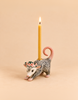The “Possum Cake Topper - Final Sale” is a hand-painted ceramic possum figurine adorned with a delicate flower crown, carrying a lit yellow candle on its back. Set against a beige background, this charming porcelain piece makes an ideal cake topper and collectible keepsake.