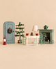 A Maileg Christmas Room Set featuring a door with a wreath, a Christmas tree, a dining table with two chairs, two tea cups, a dessert, and a fireplace with a teapot on the mantle.
