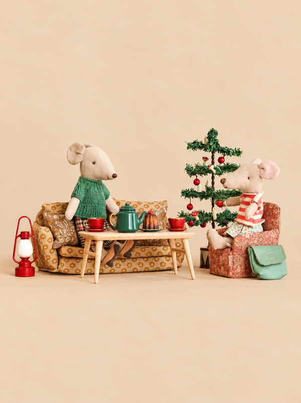 Two stuffed mice sit on miniature furniture with a Maileg Christmas Tea With Grandma Set, featuring a small coffee table, tea set, cake, and a Christmas tree.