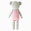 Cuddle + Kind Claire the Koala is a hand-knit grey stuffed animal with round ears, wearing a pink dress and shown from the back against a plain white background.