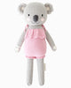 Cuddle + Kind Claire the Koala is a hand-knit grey plush wearing a pink ruffled dress, with round ears, a black nose, and blushing cheeks—crafted lovingly from sustainable fair trade materials.