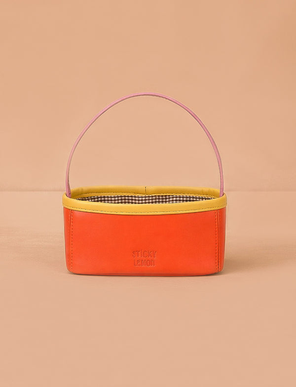 The Sticky Lemon Treasure Bag - Campfire Orange features a rectangular shape with an orange body, yellow trim, pink handle, and checked interior. "STICKY LEMON" is printed on the front—ideal as a playful treasure bag for kids.