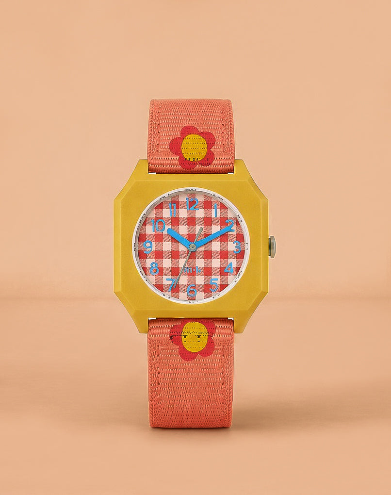 The Sticky Lemon x Mini Kyomo Watch - Flower features a yellow square case, a red and white checkered face with blue numbers, and a pink-orange fabric strap with yellow and red flower designs, shown against a peach background.