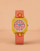 The Sticky Lemon x Mini Kyomo Watch - Flower features a yellow square case, a red and white checkered face with blue numbers, and a pink-orange fabric strap with yellow and red flower designs, shown against a peach background.