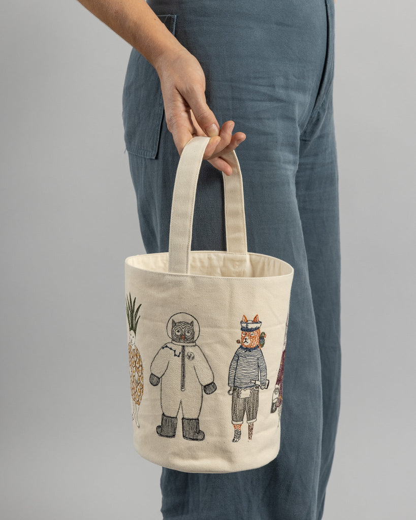 A person in blue jeans holding a Trick or Treat Small Bucket featuring embroidered designs of a haunted house and two whimsically dressed animal characters.