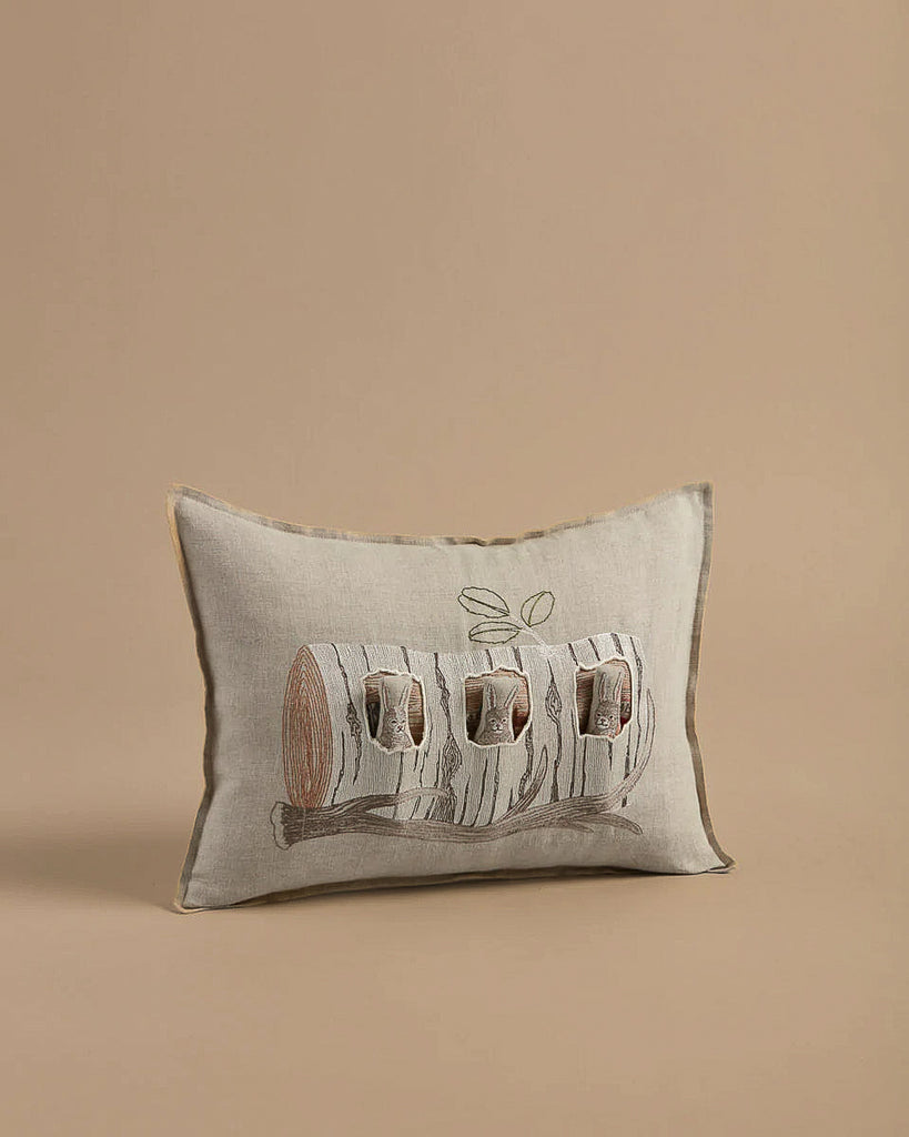 The Coral & Tusk Aspen Log Bunnies Pocket Pillow is crafted from 100% linen and features an embroidered design of three birds in a hollow log. The intricate brown, gray, and black stitching contrasts beautifully with the simple beige background.