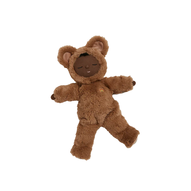 The Olli Ella Cozy Dinkum - Teddy Mini is a plush doll with brown skin, dressed in a fuzzy bear costume with hood and ears. It lies on a white background and has a peaceful, smiling expression with closed eyes.