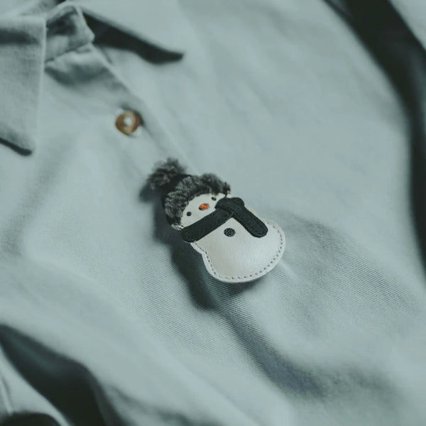 A small, handmade fairtrade Donsje Wonda Hairclip snowman ornament placed on a gray shirt, featuring detailed stitching and a tiny button eye.