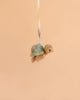 The Bukowski - Sandy Green Turtle Bag Charm features a soft plush sea turtle with a green shell, hanging from a yellow ribbon against a plain beige background, making it an adorable accessory for your bag.