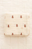 The Organic Cotton Layered Gauze Baby Blanket - Teddy (ships in one week), a soft, cream-colored blanket with a quilted texture and brown teddy bear patterns, lies neatly folded on a matching quilted surface.