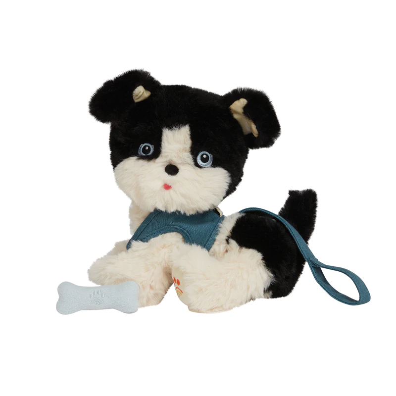 Sentence with replaced product: Plush toy from Olli Ella Dinkum Dogs, featuring a black and white puppy with overalls, sitting against a transparent background with partial black and white stripes.